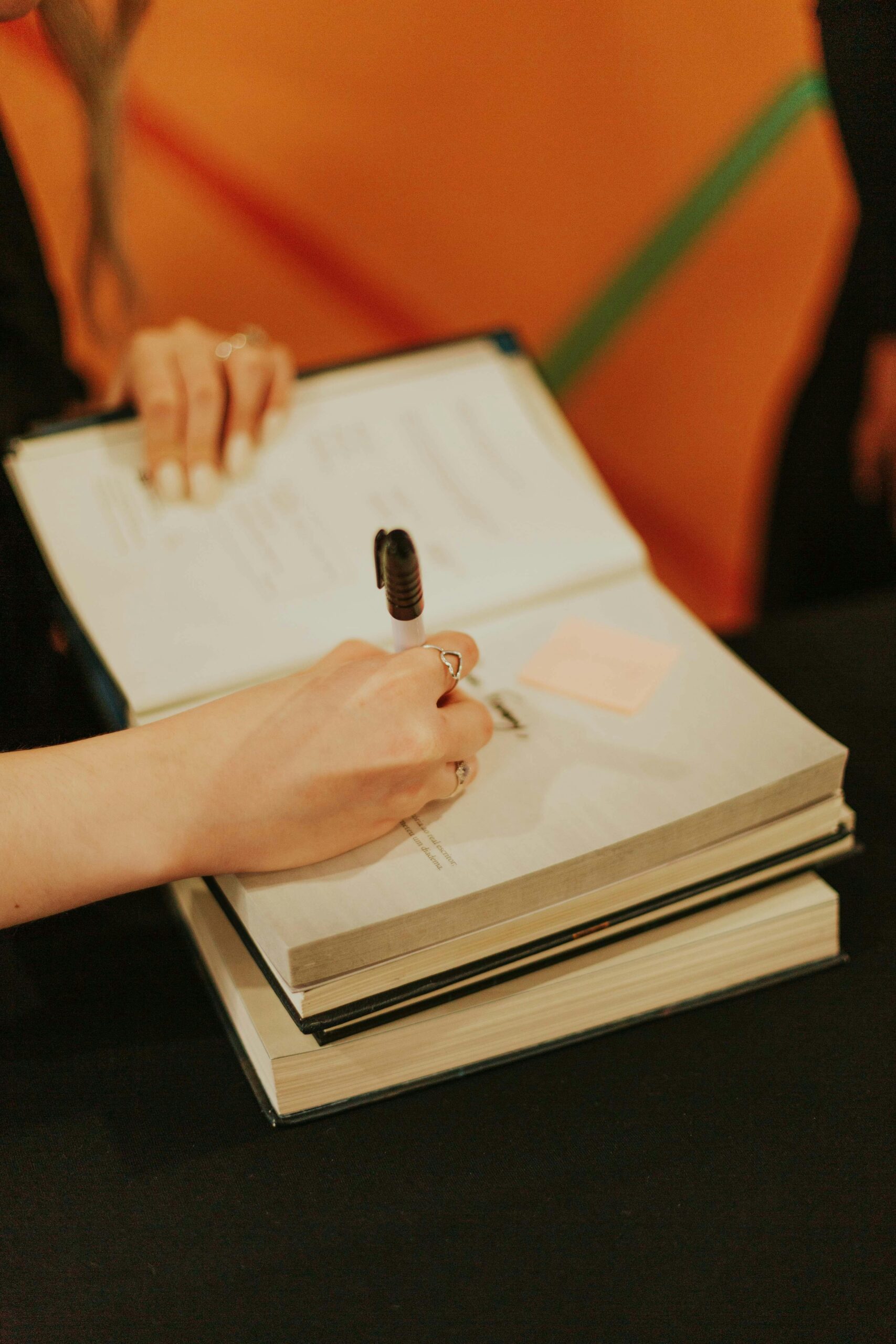 Close-up of an author signing books at a literary event, featuring orange background.
